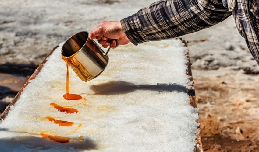 Hand pouring maple syrup on snow outdoors.