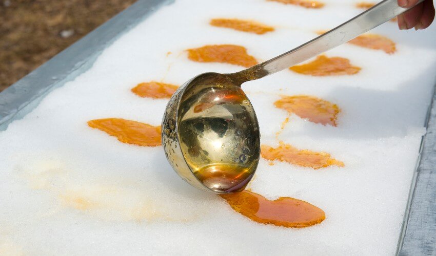 Ladle pouring maple syrup on snow.