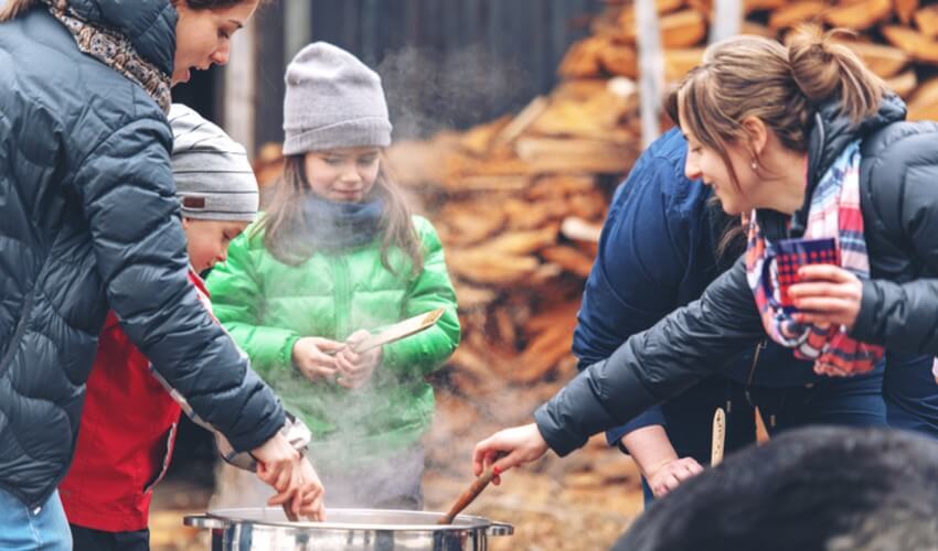 Parents and children cooking maple syrup outdoors.