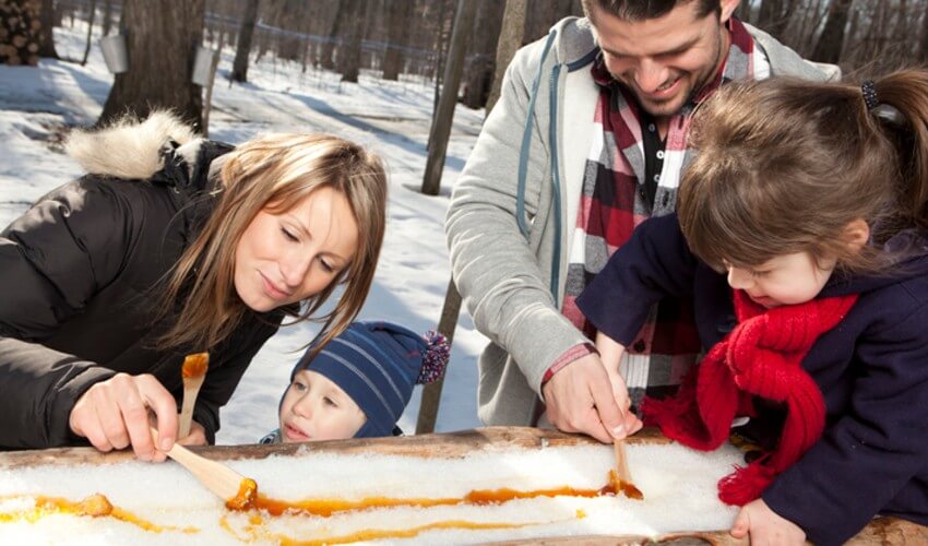 Parents rolling maple syrup on snow with their kids outdoors.