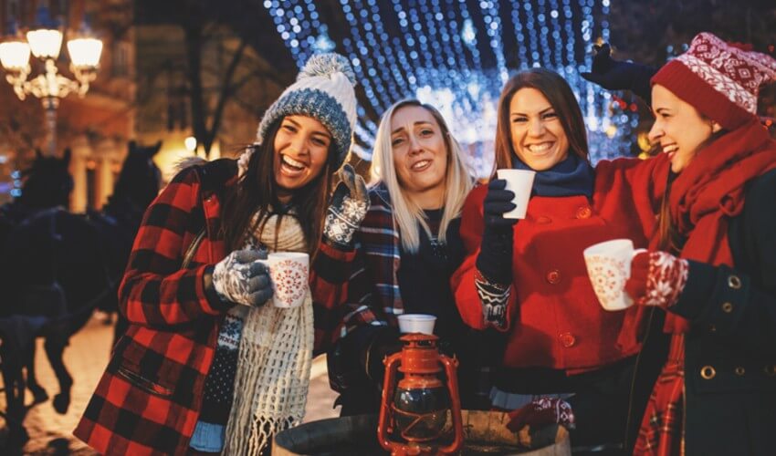 Group of happy friends cheering with hot drinks on a cold Christmas night.