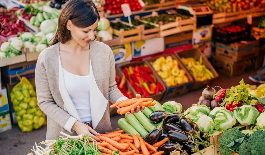 A young woman buying vegetables at a farmer’s market.