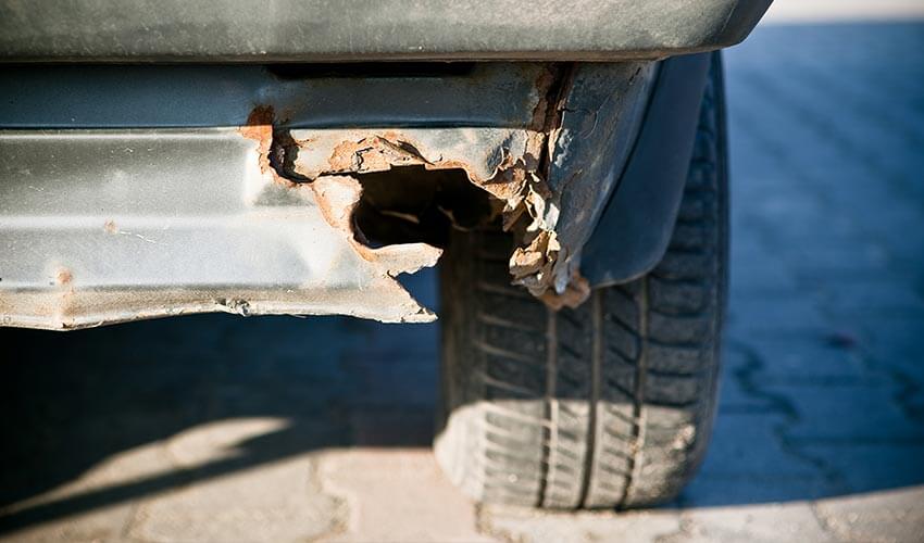 Close-up of wheel and bumper of an old, rusted car.