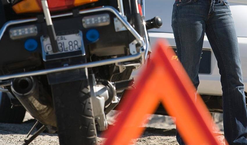 Close up of a motorcycle broken down on a road with a warning triangle placed behind it.