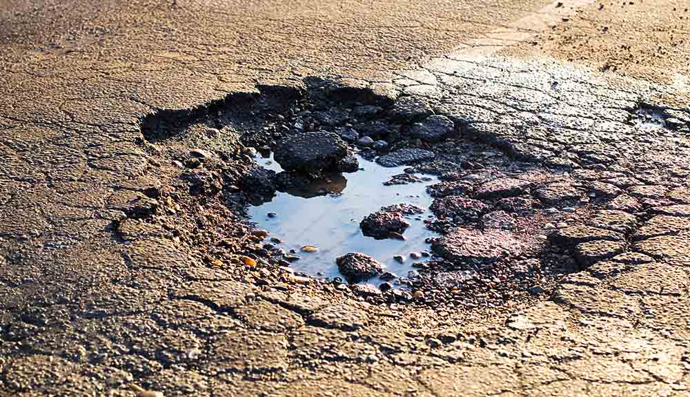 Shot of pothole filled with water and crumbled asphalt