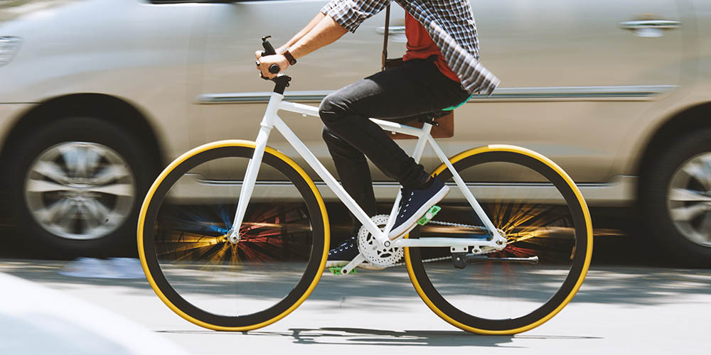 Person riding white bike with black and yellow wheels beside a light silver van 