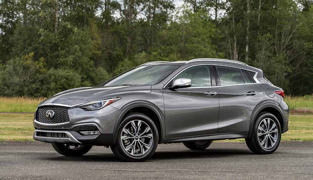 Grey Infiniti QX30 crossover SUV parked on driveway in woody area