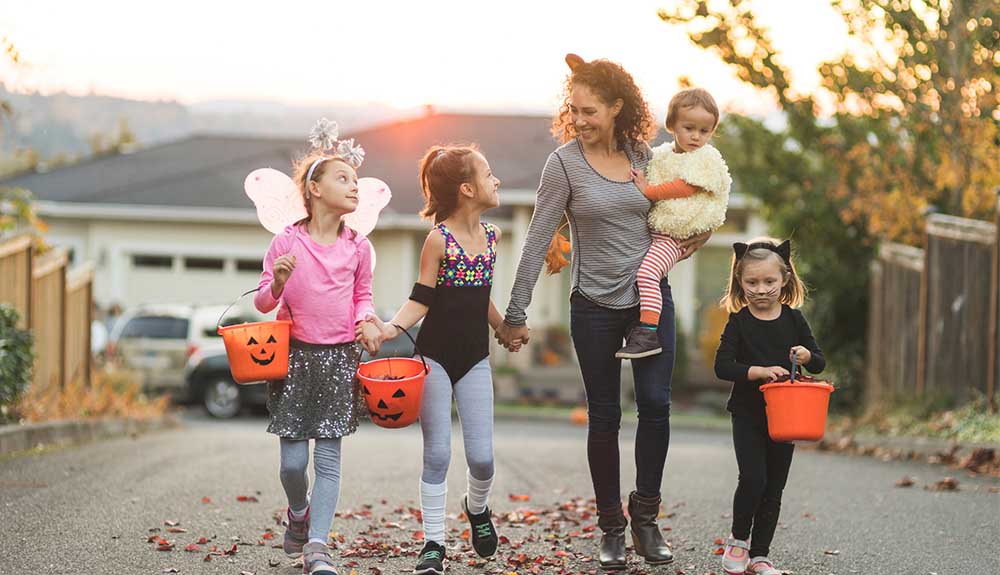 Woman with four young children dressed up as fairy and cat with buckets for trick-or-treating