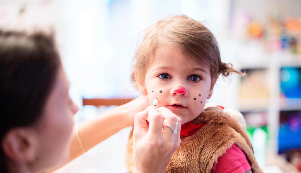 Woman painting young girl's face with whiskers for Halloween