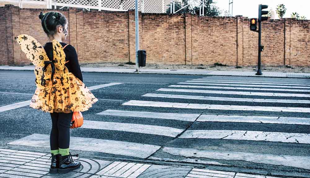 Child dressed as a butterfly for Halloween waiting to cross at crosswalk