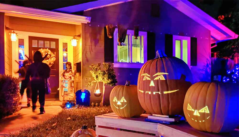 Three jack'o'lanterns on a table in front of a house with lights on at front door