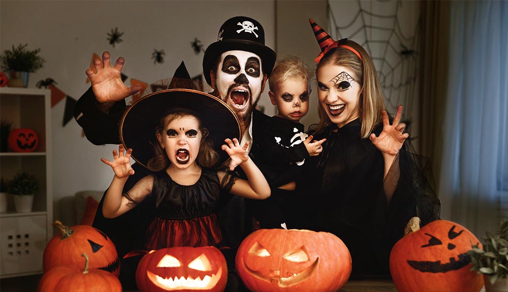 Parents and two children dressed as witches and ghouls for Halloween smiling with jack'o'lanterns