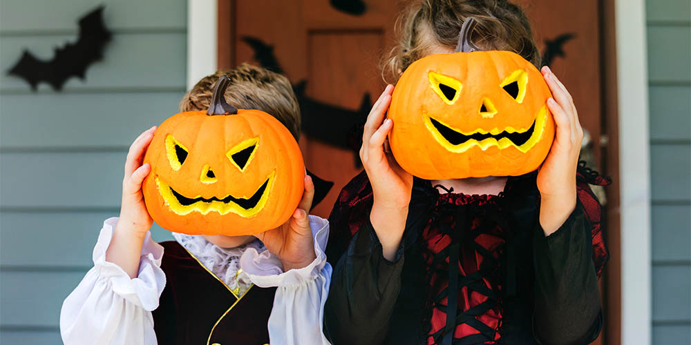 Two children covering their faces with small carved grinning pumpkins