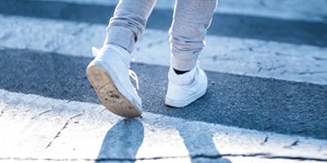 Child's feet in white sneakers walking on a crosswalk
