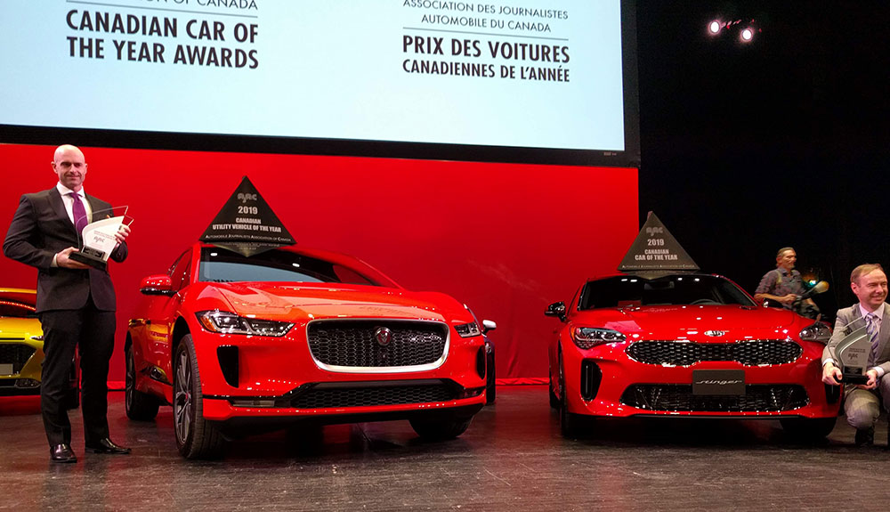 Winner's presentation ceremony for the Canadian Car of the Year and Utility of the Year car winners, a red Kia Stinger and red Jaguar I-Pace on stage with several men in suits
