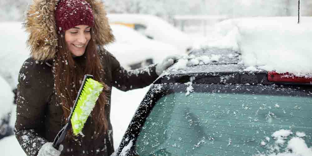 A woman scrapes her windshield on a snowy street