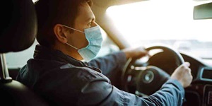 A man is shown driving with a face mask on