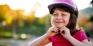 A young girl fastens the strap of her bike helmet