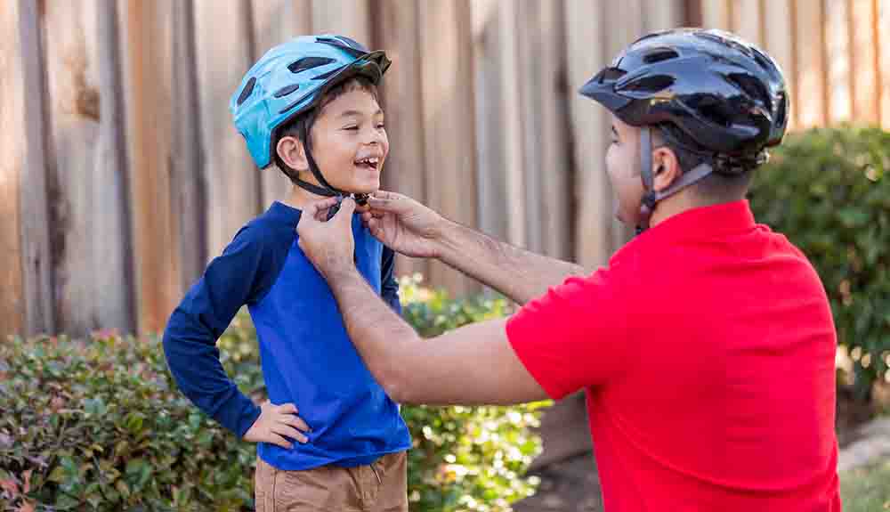 A father is shown adjusting the bike helmet on his son