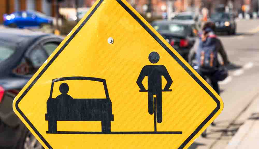 A yellow sign reminds road users to leave a one metre distance between a car and a bicycle