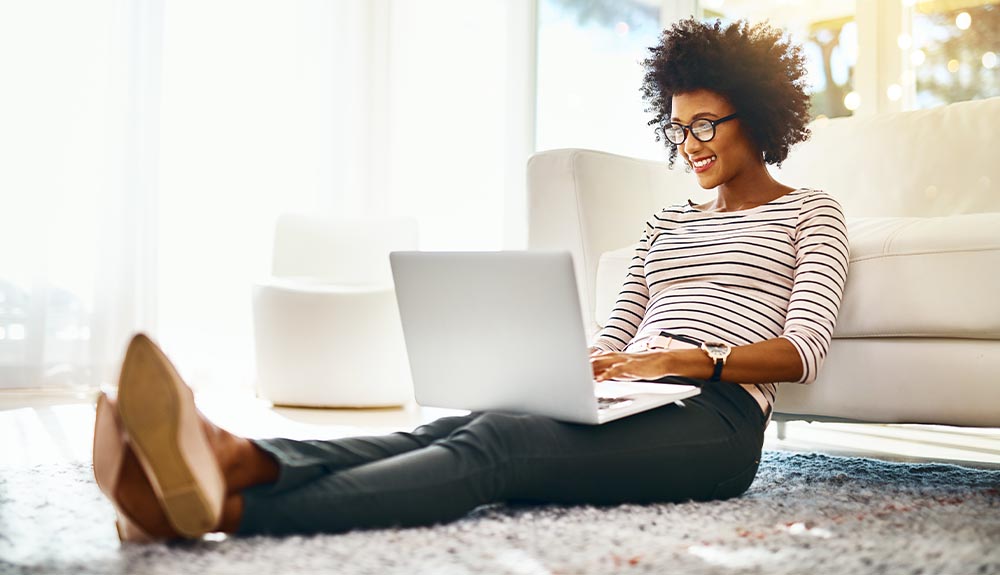 A woman looks at her laptop, while sitting on the floor in her living room