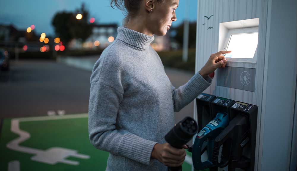 A woman is shown at an electric vehicle charging station