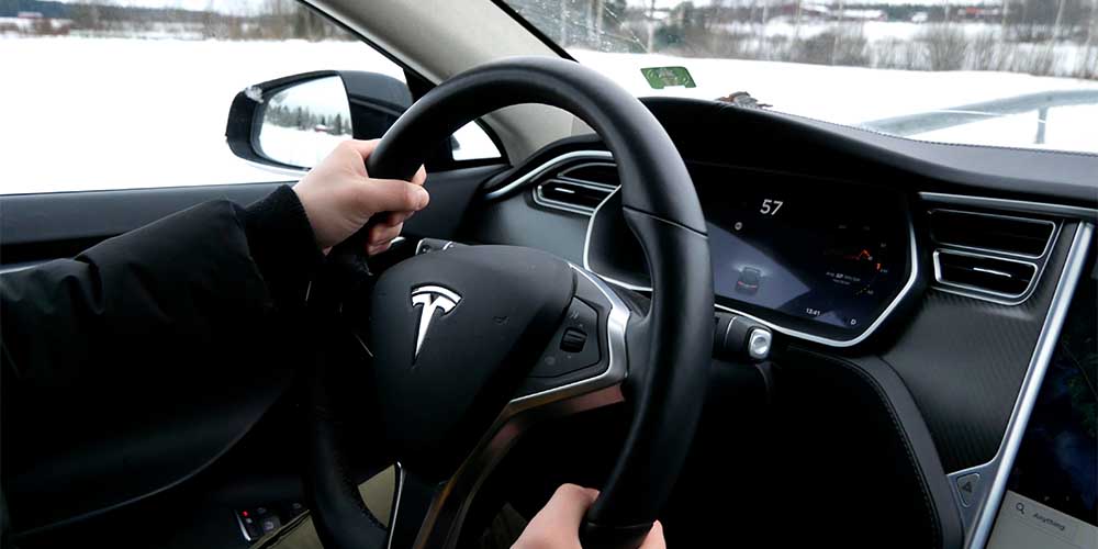 Hands are shown on the steering wheel of a Tesla electric vehicle