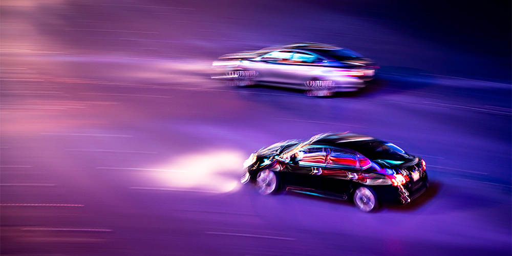 Two cars are shown racing at night on a purple background