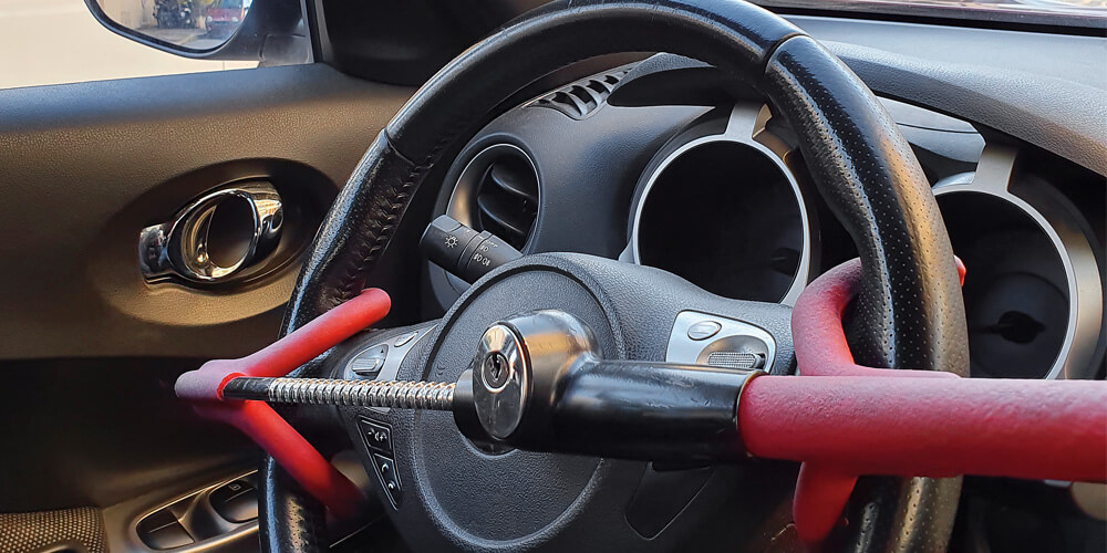 Image of a steering wheel with a red steering wheel lock on it, taken from the back seat.