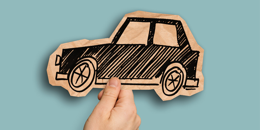 A hand holding a black drawing of a car on a piece of cardboard. The cardboard is wrinkled and cut out to outline the drawing.