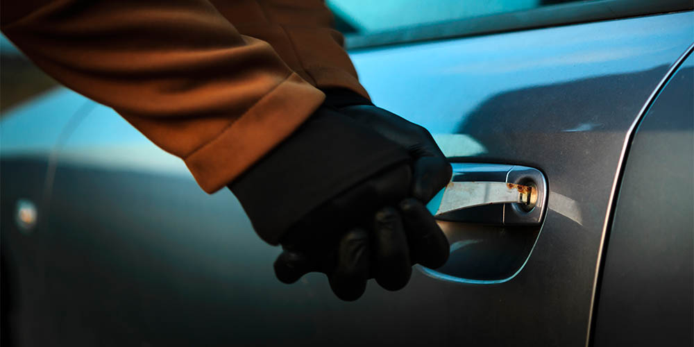 A person's gloved hands are shown on the door handle of a silver car