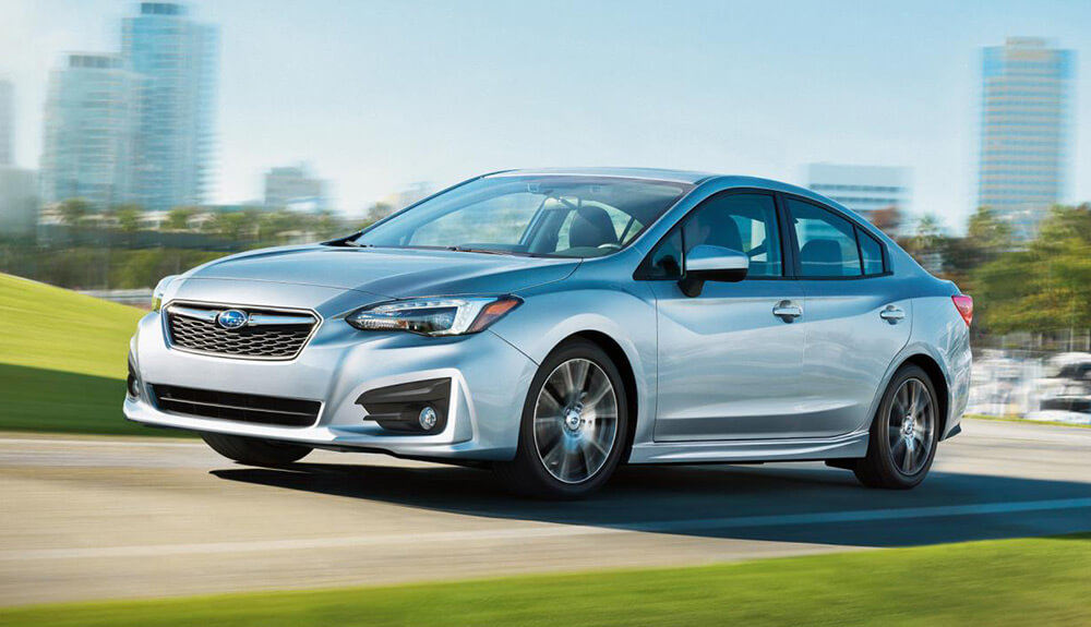 Silver Subaru Impreza Sport drives down a suburban road with grass on either side of it