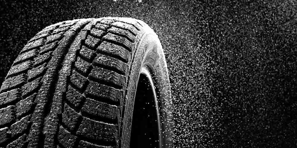 Closeup shot of winter snow tires with deep treads, dramatically spraying snowflakes away