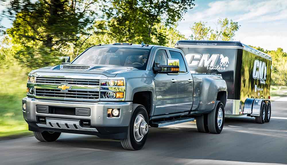 Chevy Silverado 3500HD truck driving down a country road with branded trailer attached