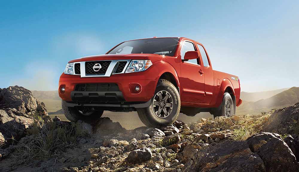 Red Nissan Frontier driving up a rocky hill