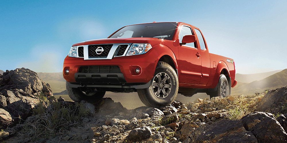 Red Nissan Frontier pickup truck drives on a rocky road