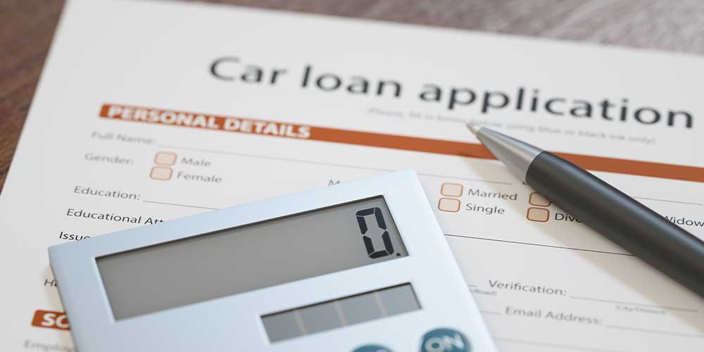 A calculator with the number at 0 is sitting on top of a car loan application form. There is also a pen on top of the form.