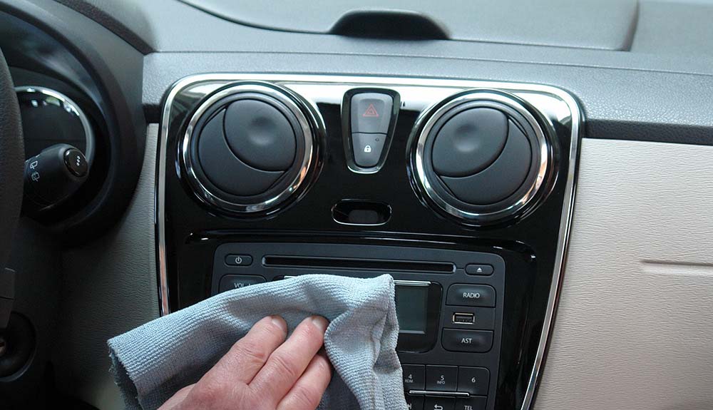 Hand wiping the dashboard of the interior of a car