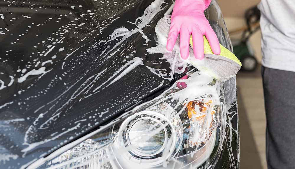 Super soapy hood being scrubbed with a sponge by a man wearing a pink glove
