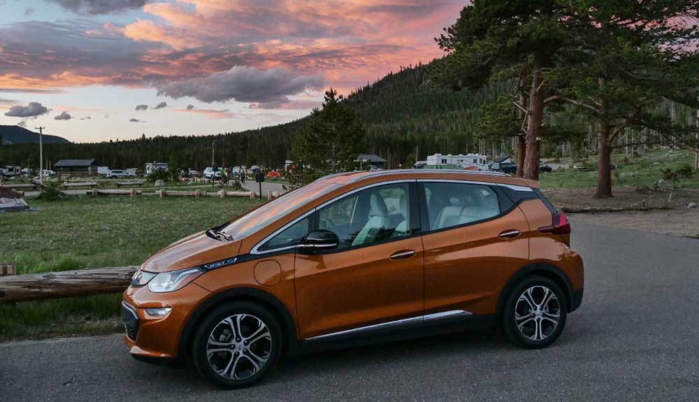Orange electric vehicle parked on the side of the road with a beautiful sunset in the background