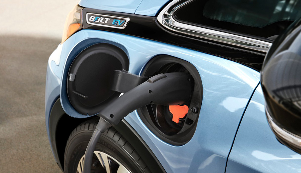 Close up of Chevy Bolt charging with electric handle plugged in by where a traditional gas tank would be