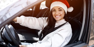 A woman wearing a white sweater and a Santa hat is sitting in the driver seat wearing a seat belt.