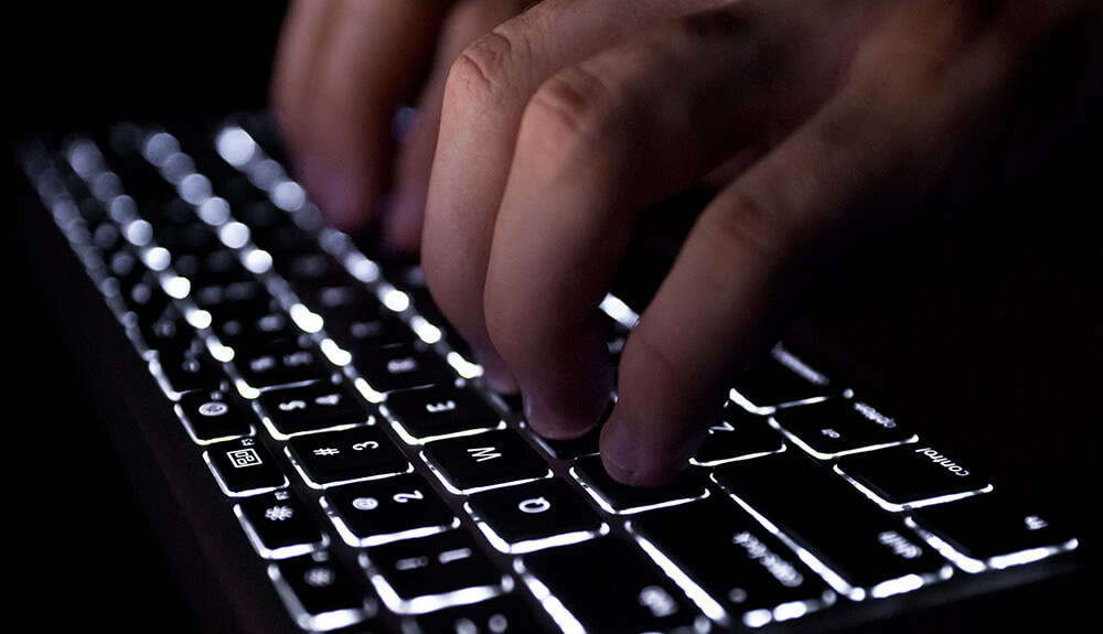 Hands typing on a black lit up keyboard
