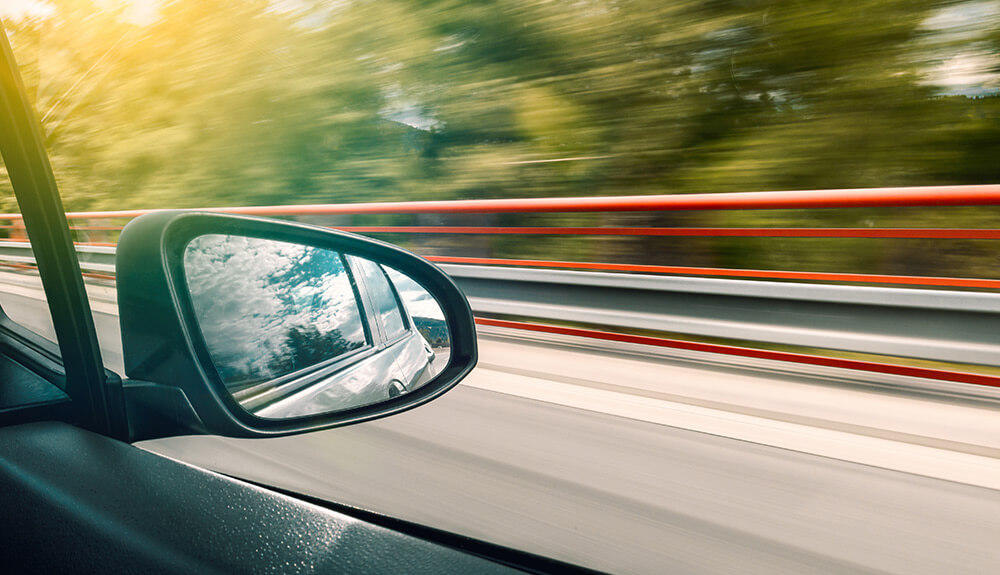 Closeup shot of passenger side window with cloudy blue sky reflected, blurred background indicating the speed of the vehicle