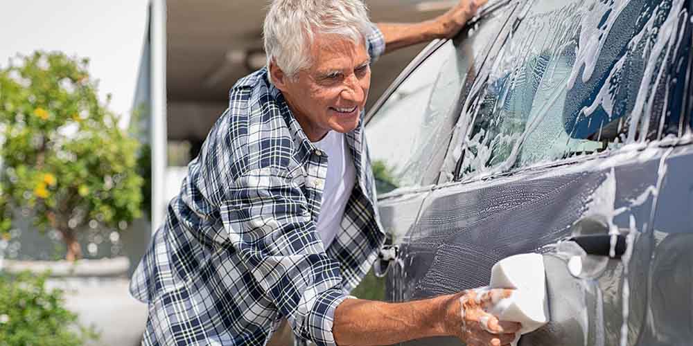 A man in a plaid shirt washes his car outdoors