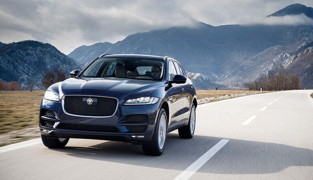 Black Jaguar F-Pace driving down a freeway with mountains in the background