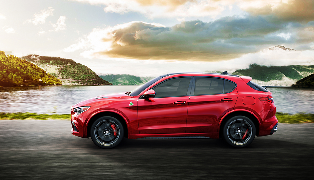 Bright red sporty-looking Alfa Romeo Stelvio Quadrifoglio crossover speeding beside a lake on a cloudy day near sunset