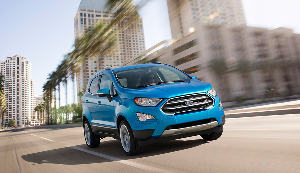 Bright blue 2018 Ford Eco Sport driving speedily down urban freeway with low rise and high rise buildings in background