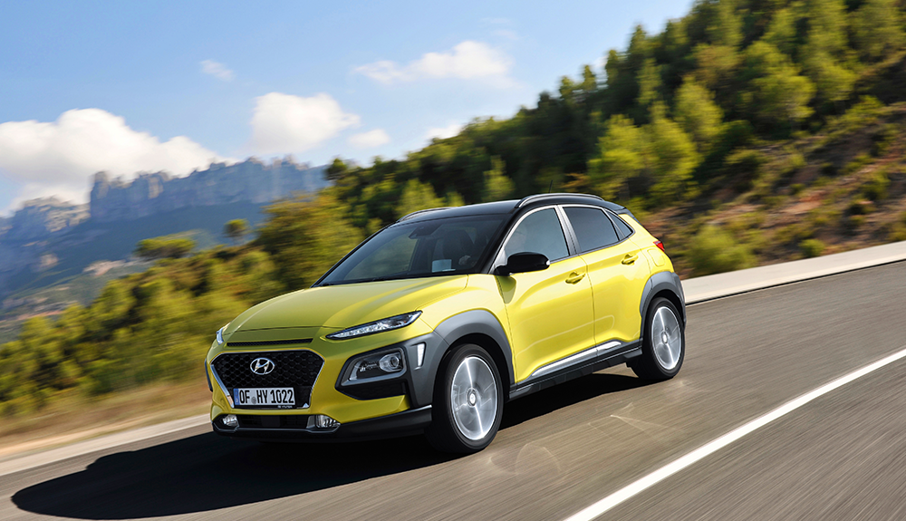 Lime green 2018 Hyundai Kona driving down freeway with lush foliage on hill in background