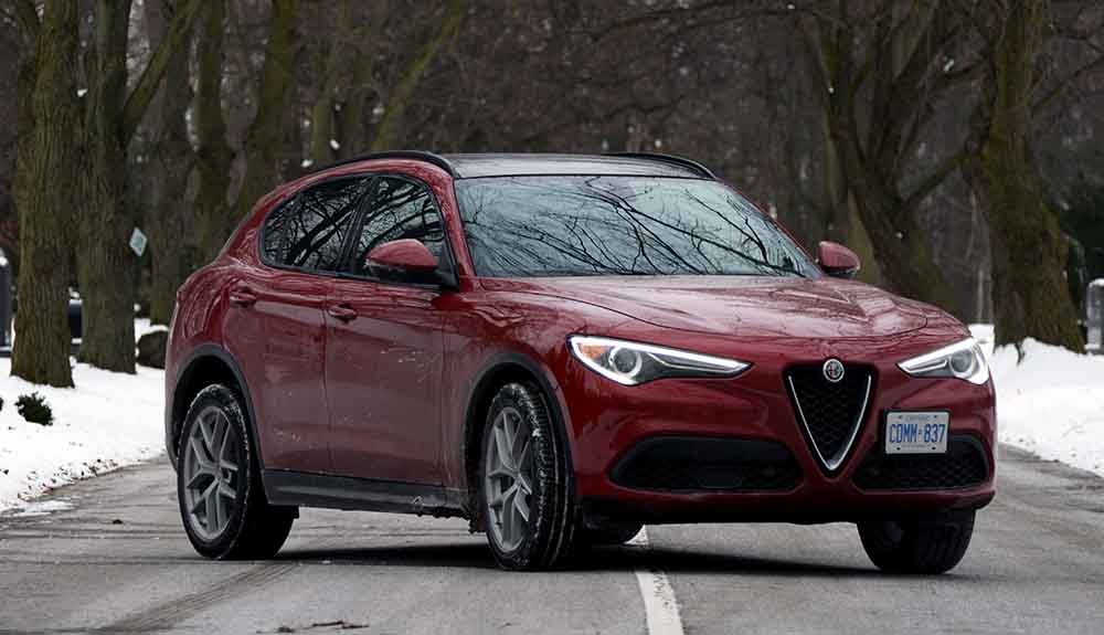 Dark red 2018 Alfa Romeo Stelvio parked on a paved winter street in heavily wooded area